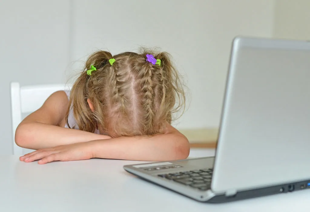Little girl resting her head on the table in front of a laptop