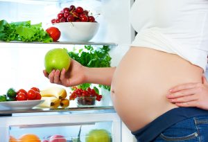 A pregnant woman picking a fruit from the refrigerator