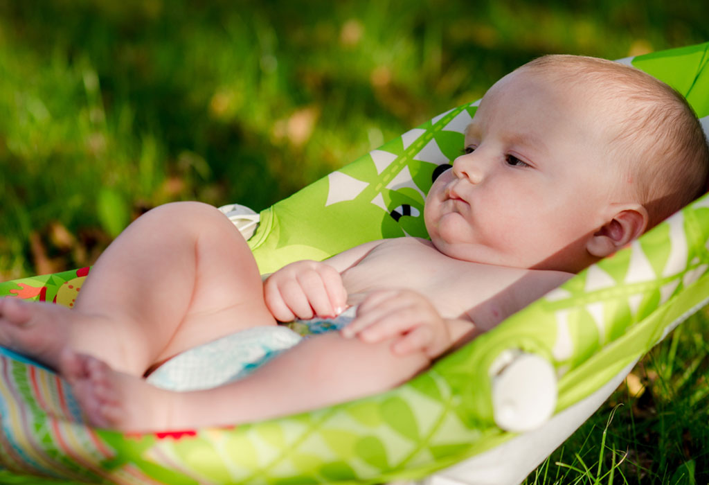 A baby laying in the rocking chair on the grass in the sunlight