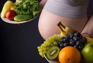 A pregnant woman holding a plate of fruits and vegetables