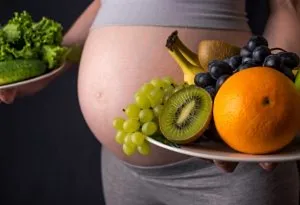A pregnant woman holding a plate of fruits