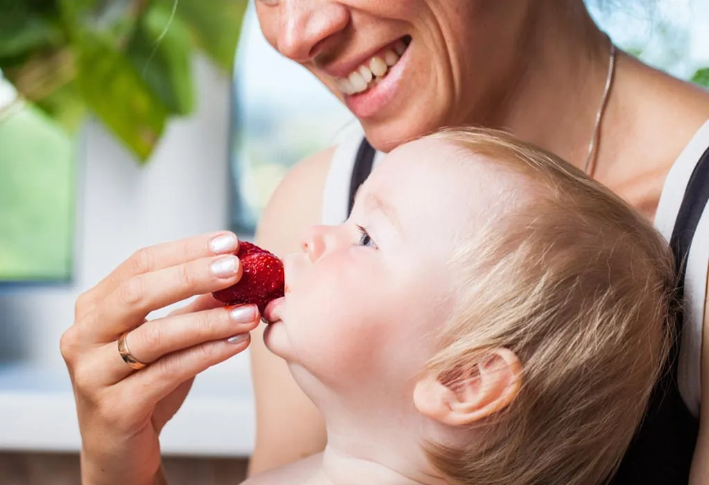 A mom feeding strawberry to her child
