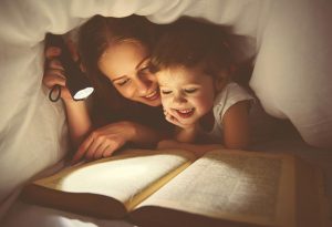 A mother and daughter reading a book under the flashlight at night