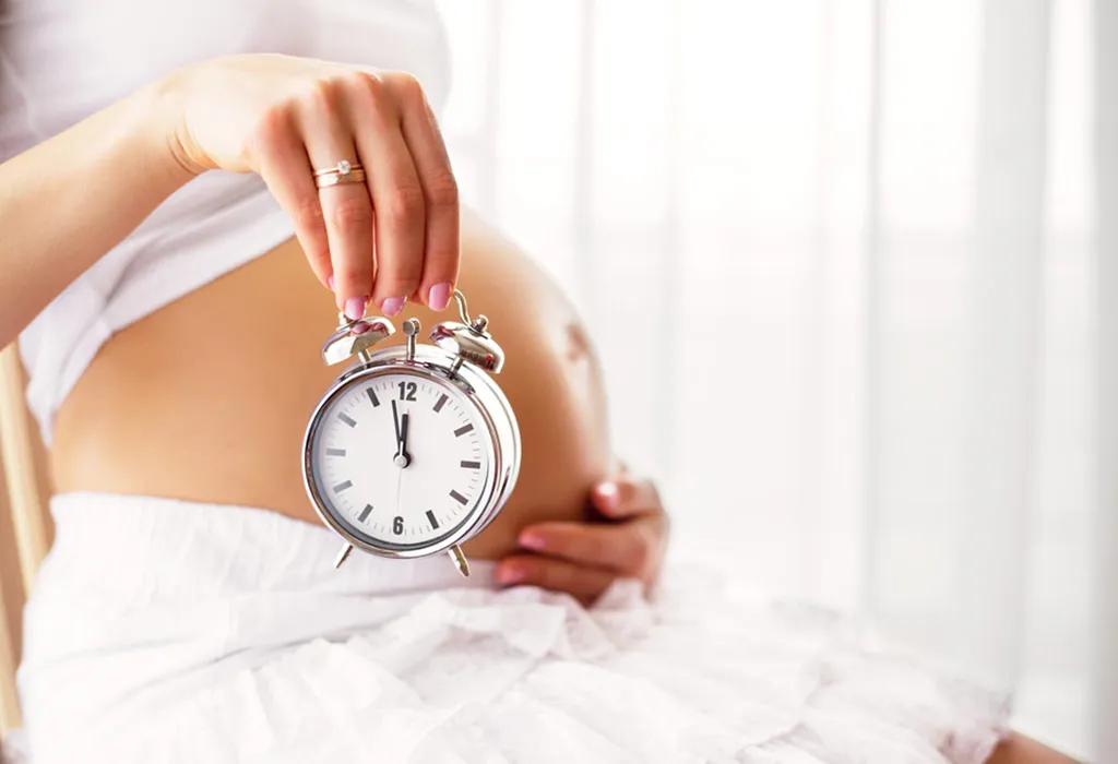 A pregnant woman holding a clock near her belly