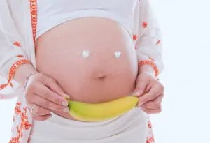 A pregnant woman holding a banana close to her belly