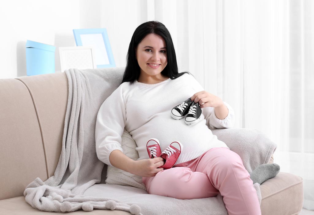 A pregnant woman holding two pairs of shoes close to her belly