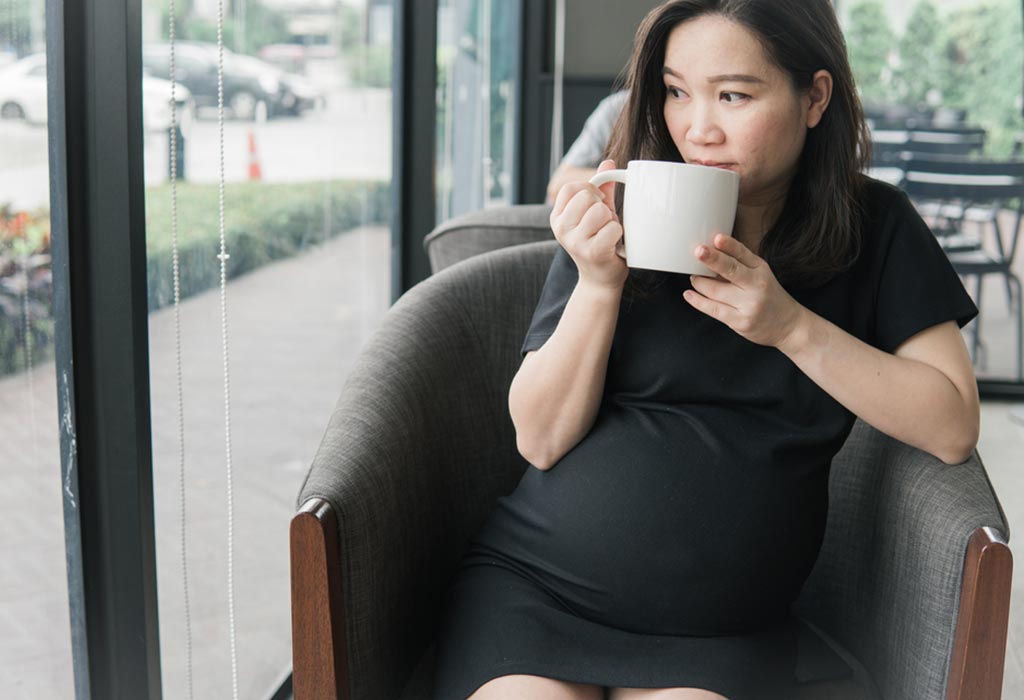 A pregnant woman drinking a cup of coffee