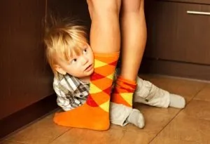 Socially awkward child hiding behind mother's legs