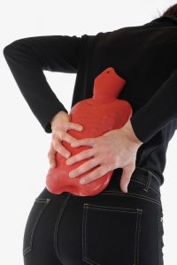 A woman using a hot water bag to cure back pain