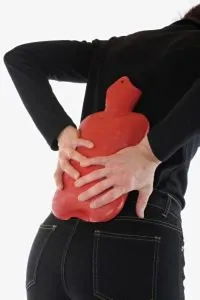 A woman using a hot water bag to cure back pain