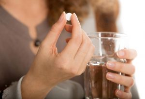 A woman holding a pill and a glass of water