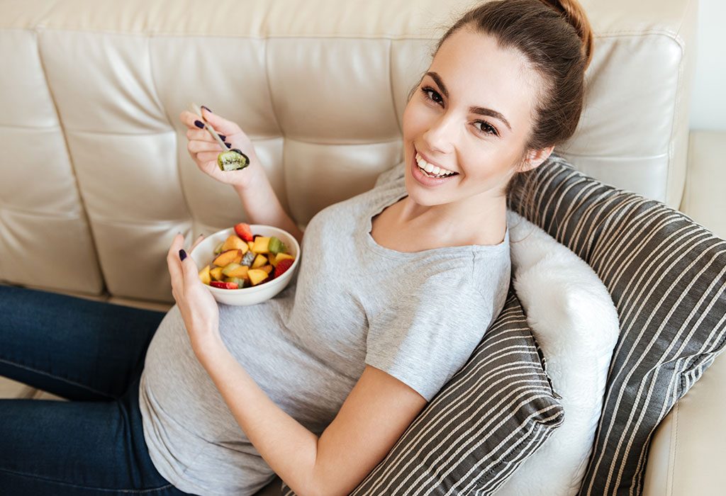 A pregnant woman eating a healthy meal while sitting on the couch