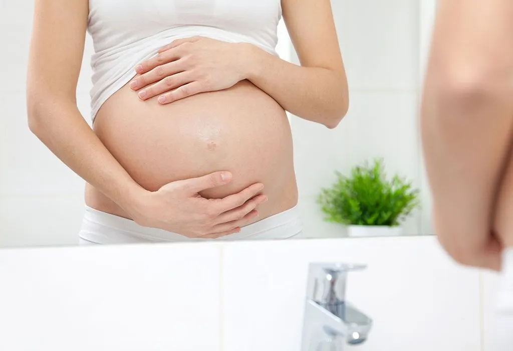 A pregnant woman looking into the bathroom mirror