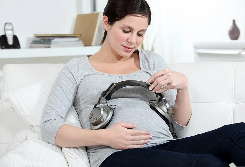 A pregnant woman places headphones on her belly