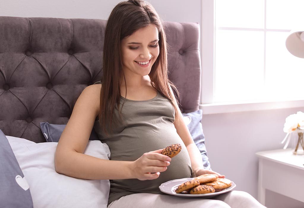 Pregnant woman eating biscuits in bed