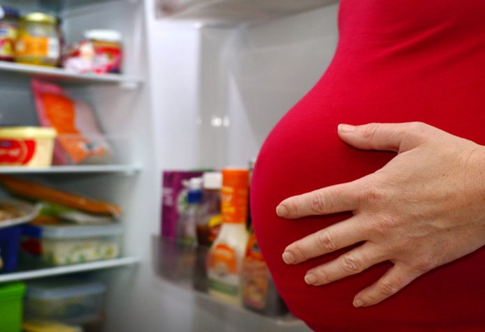 A pregnant woman standing near the refrigerator