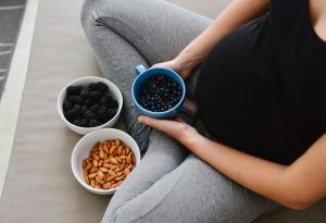 A pregnant woman sitting with a bowl of almonds and fruits