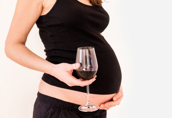 A pregnant woman with a glass of red wine in her hand