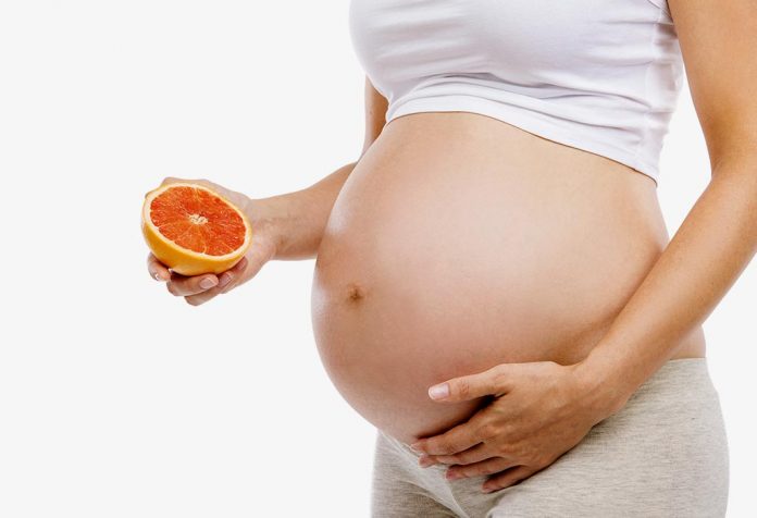 A pregnant woman holding a grapefruit near her belly