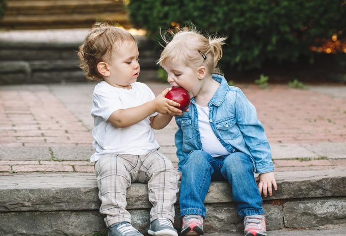 A little boy sharing an apple with a little girl