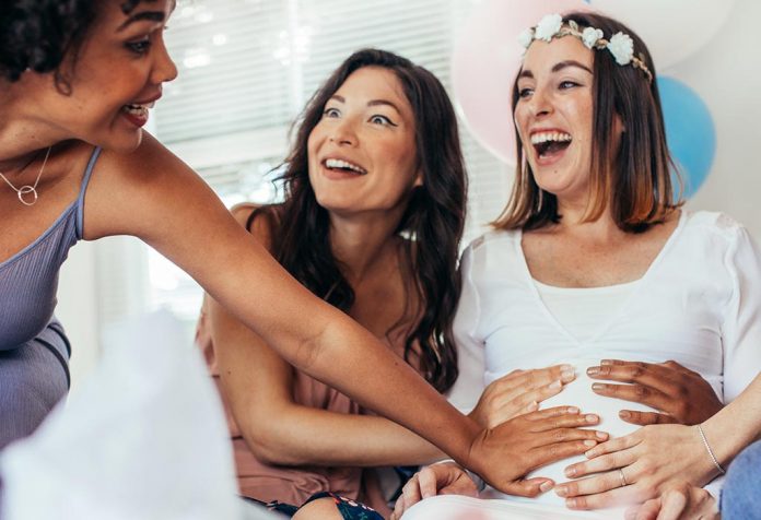 Excited young women touching their pregnant friend's belly
