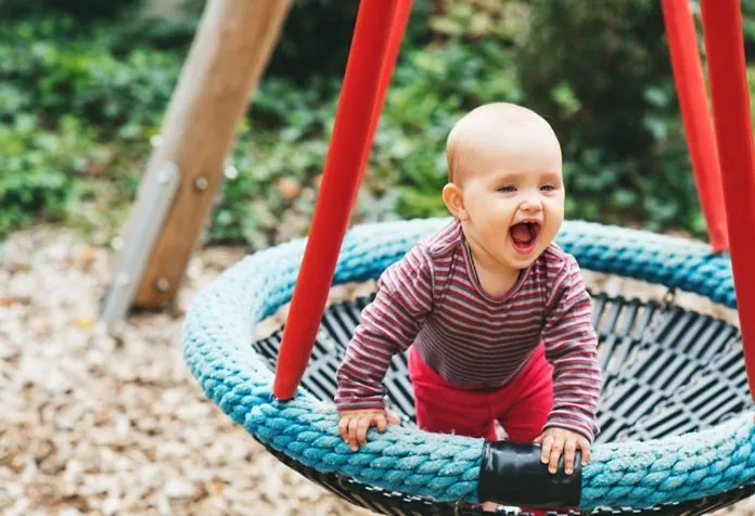 A nine month-old baby playing on the swing