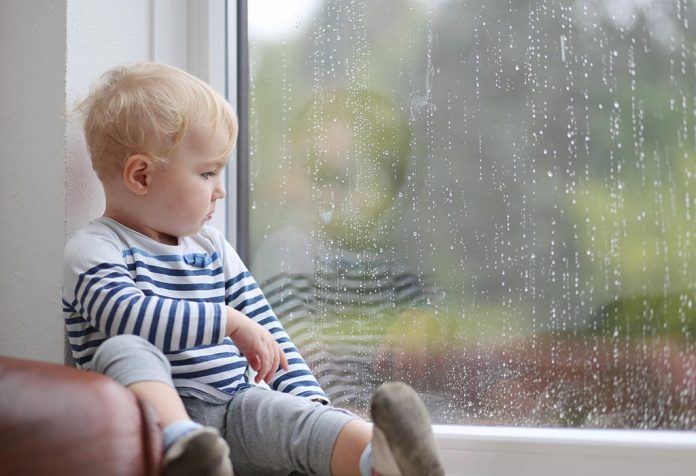 A little boy staring at the rain through the window