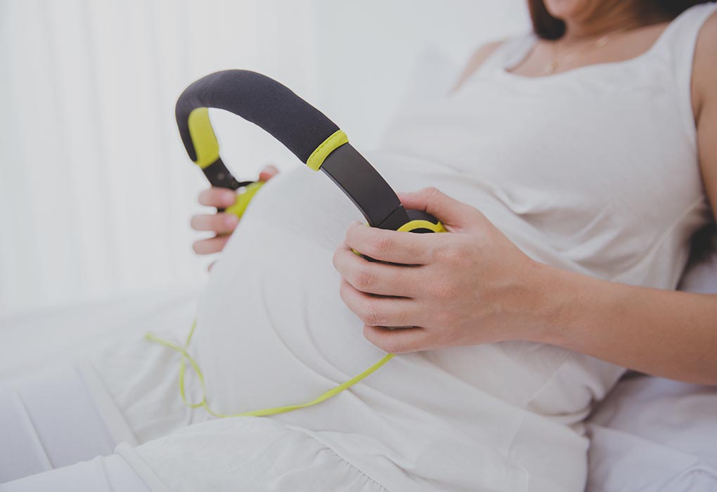A pregnant woman with headphones in her hands