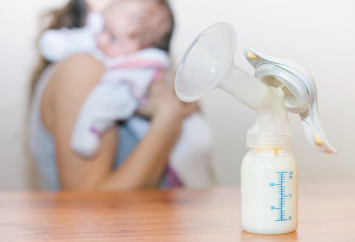 worried mother standing with her baby behind a bottle of expressed milk