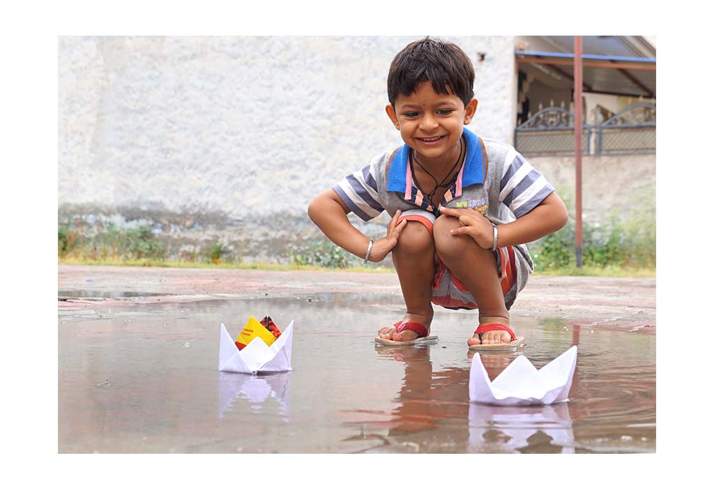 बारिश में कागज का नाव बनाकर खेलता बच्चा